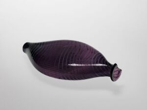  A stylized glasswork fish with a deep purple color and subtle darker stripes, showcasing a smooth transition from a broader body to a narrow tail, set against a light grey background.