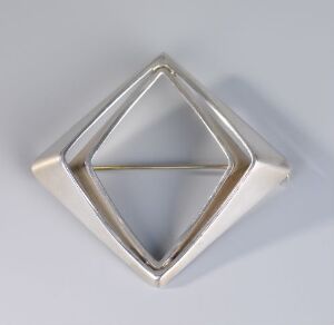  A polished hand-forged sterling silver geometric jewelry piece by PLUS, featuring a larger hollow square diamond shape with a smaller inverted diamond shape nested inside, displayed against a soft, light-colored background.