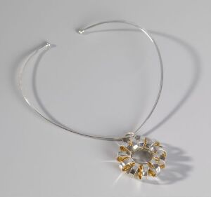  Anna-Greta Eker designed necklace with a silver circular pendant having a radiant, twisted, and interior gilded design, set on a sleek silver collar, showcased against a neutral background.