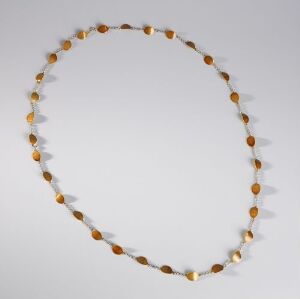  A circular necklace with alternating golden semi-transparent round beads and smaller cream-colored disc beads laid out against a light gray background.