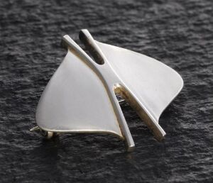  A sterling silver brooch with an abstract design by Erling Christoffersen, featuring a curved triangular shape intersected by a rod with a small gold detail, set against a textured dark background.