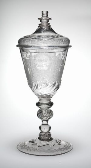  A clear, blown glass goblet with engraved decoration named "Sophia Dorothea-pokalen" by Heinrich Gottlieb Köhler. The goblet features a footed base, a decorative stem, a tapered body with intricate engravings, and a matching lid, all displaying the fine craftsmanship.