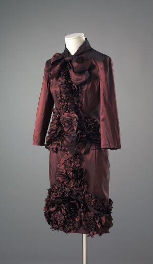  A detailed burgundy two-piece garment with ruffles displayed on a featureless mannequin against a neutral gray background.