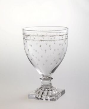  A clear cut crystal goblet with a faceted stem and octagonal base, etched with small dots, filled with a translucent liquid, set against a light background.