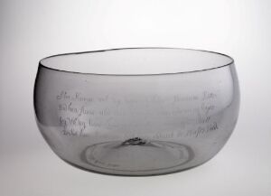  A subtle gray-tinted transparent glass bowl with faint etchings, resting on a plain light gray background. Artist name and title are unknown.
