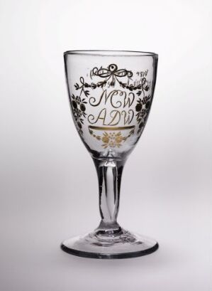  A decorated clear glass goblet with intricate designs on the upper half stands against a plain, light background.