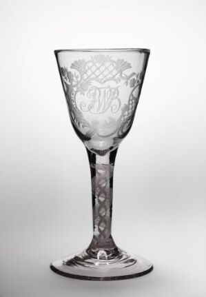  An elegant clear glass goblet with detailed etching, including decorative elements on the stem and a monogrammed design on the bowl, set against a light-grey background.