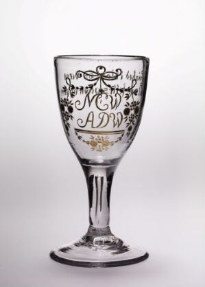  An elegantly designed clear glass goblet with a monogrammed motif featuring ornate black patterns, possibly initials, on its upper bowl, set against a plain light grey background.