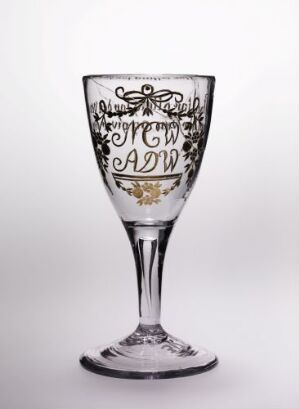  An elegant clear glass goblet with intricate black decorative patterns, including scrolls and floral designs, around the middle of the bowl, set against a plain light background.