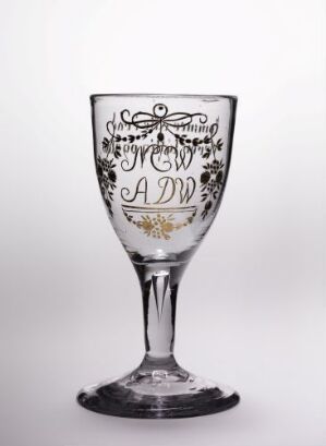  A decorative glass goblet with a detailed black monogram design of intertwined letters "A" and "W" surrounded by ornate scrollwork, on a light gray background. The title and artist's name are unknown.