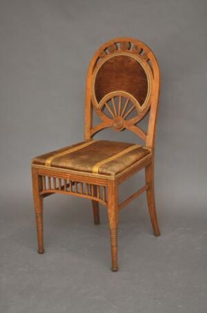  An antique wooden chair with a sunburst pattern on the high, oval-shaped backrest, presented on a plain gray background. The chair has a warm, golden brown finish and slender, ornamented legs.