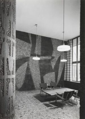  Black and white photograph of a modernist interior space with a large abstract wall mural, a central table surrounded by chairs, and three hanging light fixtures. Large window to the right casts light across the patterned floor.