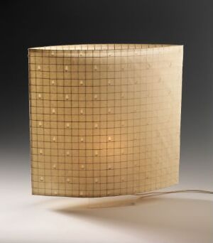  A square-shaped paper lamp by Irina Pått with a grid pattern illuminated from within, casting a warm, gentle glow on a neutral dark background with the power cord slightly visible at the base.