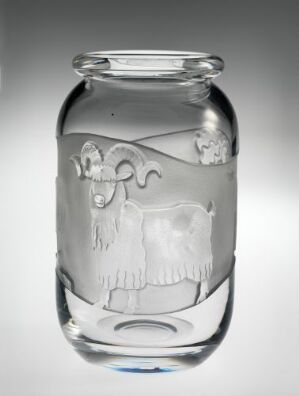  A clear glass jar with a decorative engraved heraldic crest featuring a shield, helmet, and acanthus motifs on a gradient gray background.