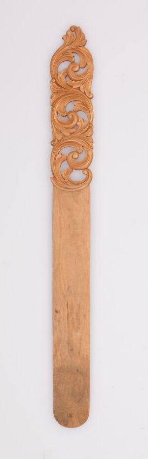  A slender, intricately carved wooden object with traditional motifs on a light-colored background. Artistname and title remain unknown.