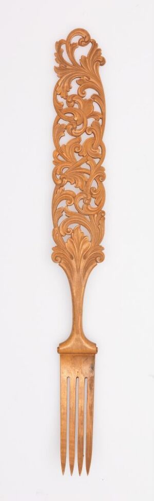  An ornate wooden fork with an intricate, lace-like carved handle in a warm, golden-brown hue against a plain background.