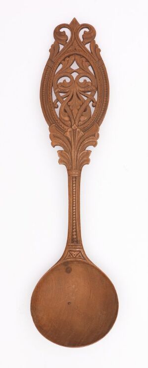  An ornate wooden spoon with a delicate, symmetrical cut-out design on the upper half of its handle, displayed against an off-white background. The spoon has a warm, brown color with a circular bowl at the bottom and an elegantly tapered handle that culminates in a pointed, oval silhouette.