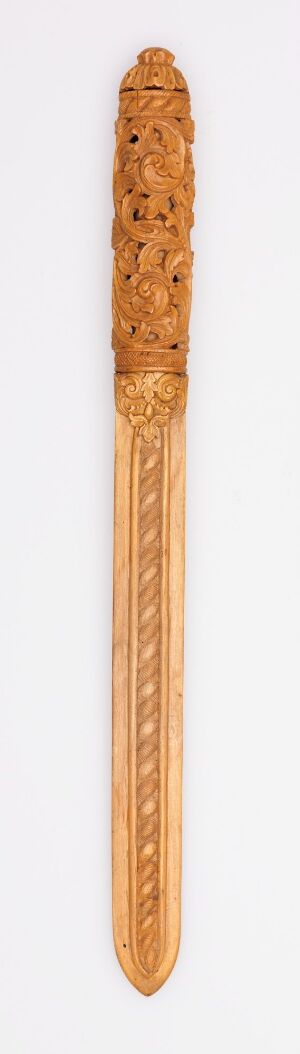  A vertical image of a slender, elongated object, likely wooden, with intricate carvings at the top and ribbed lines along its length, displayed against a light background. Artist name and title are unknown.