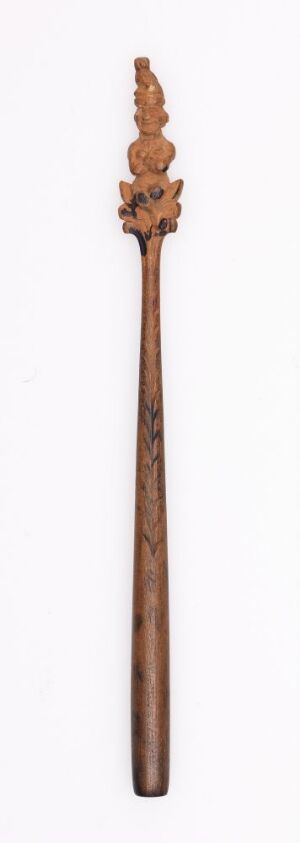  A slender, elongated wooden wand with ornate floral carvings at the top end, against a plain, light background, showcasing the intricate details and craftsmanship.