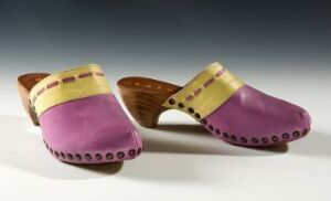  A pair of traditional wooden clogs painted in deep purple with mustard yellow bands at the top, set against a grey to white gradient background.