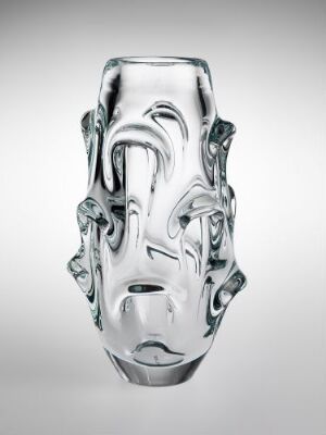  A clear glass vase featuring stylized faces molded into the design, standing against a plain, light gray background, with interplay of light casting highlights and shadows that emphasize the artistic contours of the vase.