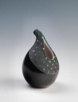  A matte black, organically shaped vessel with a curved neck and a pattern of small green speckles on a light to white gradient background.