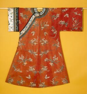  A traditional Asian-style robe with a reddish-orange silk fabric, adorned with bird and floral patterns in white, blue, and lighter orange, and a contrasting detailed collar and front edging, against a plain background.