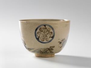  A ceramically crafted bowl with a natural sand-colored glaze, adorned with blue and brown intricate leafy designs and small creatures in flight around the exterior.