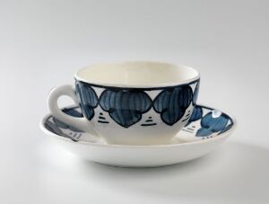  A cup and saucer set designed by Andreas Schneider. The ceramic pieces are glazed and decorated with hand-painted blue floral patterns on a white background. The cup has a single handle and is accompanied by a matching saucer with a similar blue pattern around the rim.