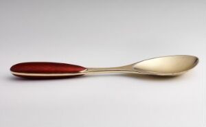  A spoon with a silver-colored bowl and a handle with a deep burgundy red inlay, resting on a neutral light background.