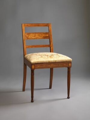  An elegant wooden chair with a medium-brown finish, featuring a decorative carved top bar on the backrest, and a cushioned seat upholstered in pale yellow fabric with a subtle floral pattern against a neutral background.