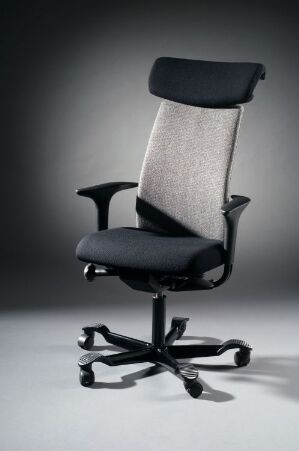  An ergonomic office chair with a black base and armrests, a padded black seat, and a grey woolen upholstered backrest highlighted by a headrest at the top, designed by Peter Opsvik.