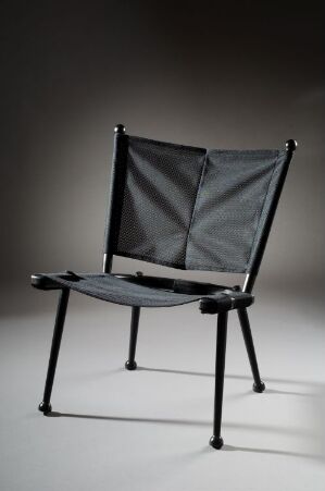  A varnished and stained laminated wood chair titled "Safari" by Naturellement A/S, featuring a sleek black frame with dark grey textile for the seat and backrest, displayed against a graded background that shifts from light to dark.