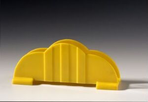  A lemon-yellow plastic tableware item with a symmetrical, ribbed design, reminiscent of an arched napkin holder, standing on a white surface against a grey gradient background. Artist and title are unknown.