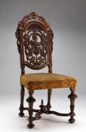  An antique wooden chair with ornate back carvings and a faded golden yellow upholstered seat, set against a gradient gray background.