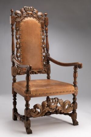  An intricately carved antique wooden chair with tan upholstery on the seat and backrest, set against a neutral background, demonstrating elaborate craft and historical design.