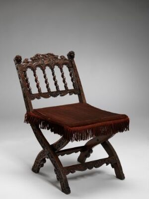  A dark walnut wooden folding chair titled "Klappstol" by an unidentified artist, featuring intricate carvings and relief work, with a polished finish and a red velvet upholstered seat with fringes, set against a gray background.