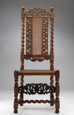  An antique dark brown wooden chair with a tall, caned backrest, turned posts, and an intricate stretcher, against a neutral background.