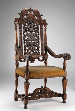  An antique wooden armchair with elaborate openwork carvings on the backrest and a faded golden upholstered seat, set against a light grey background.