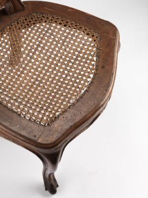  Close-up of an antique wooden chair with a woven cane seat, showcasing the rich warm brown tones of the wood and contrasting beige of the intricate weave, with a focus on the textures and elegant curving details.