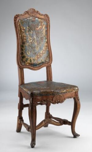  An elaborately carved antique wooden chair with a high backrest, decorated with a floral upholstered tapestry, set against a neutral grey background.