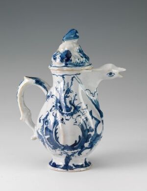  A white-glazed fajanse coffee or teapot with hand-painted cobalt blue decorations, featuring a bird’s beak-shaped spout and a decorative knob on the lid, against a neutral background. Artist unknown.