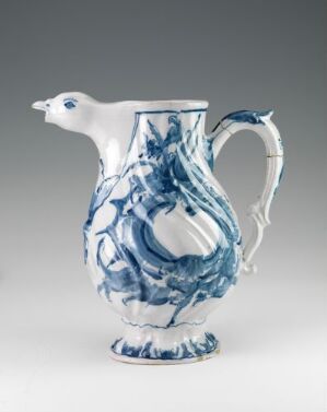  A white-glazed fajanse jug by Herrebøe Fajansefabrikk with hand-painted cobalt blue abstract decorations, featuring an ornate handle and a spout shaped like a bird's head, against a neutral grey background.