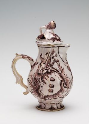  An elegant white-glazed fajanse jug with hand-painted manganese-red baroque-style decorations, featuring a curled handle and ornate lid, artist unknown.