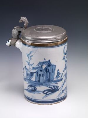  A cylindrical ceramic jar with a metallic lid and handle, featuring cobalt blue pastoral scene paintings on a white background and handle shaped like a mythical creature.