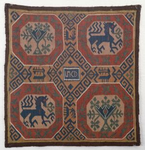  An antique square textile with a symmetrical design featuring stylized trees and prancing horse figures within a terracotta red, green, and sandy beige color scheme on a muted gray background. Artist and title unknown.