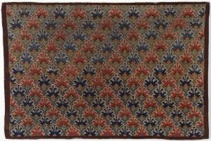  A woven textile piece titled "Skybragd" by an unidentified female artist, showcasing a pattern of stylized floral motifs in shades of blue, red, and peach on a dark background, exemplifying traditional weaving techniques.