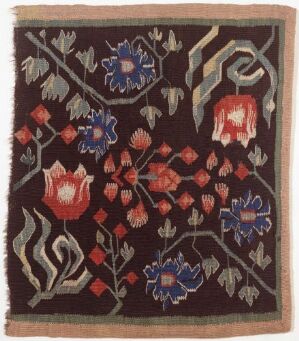  A square fabric piece with intricate floral patterns in shades of red, blue, and green on a dark brown background, surrounded by a lighter beige border, suggesting an ornate rug or tapestry.