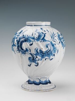  A white-glazed fajanse vase by Herrebøe Fajansefabrikk with hand-painted cobalt blue decorative patterns, featuring Rococo or Baroque style scrolling motifs and stylized foliage on a rounded body with a small base.