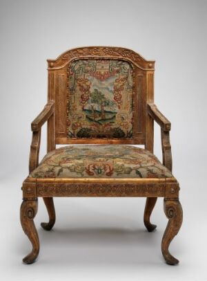  Antique ornately carved wooden armchair with tapestry upholstery depicting a classical scene in muted greens, reds, and beige, set against